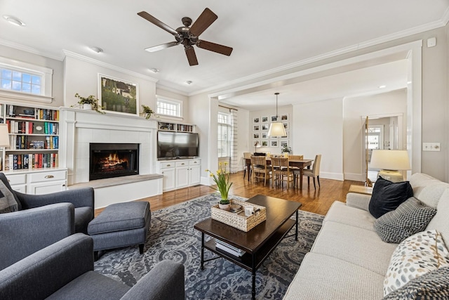 living room with a wealth of natural light, ornamental molding, ceiling fan, and wood finished floors