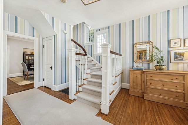 staircase with wallpapered walls, wood finished floors, and baseboards