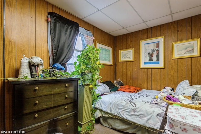 bedroom featuring wooden walls, a drop ceiling, and carpet floors