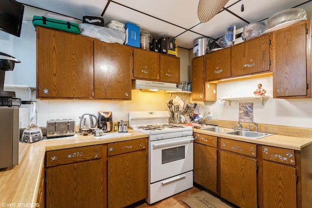 kitchen featuring white range with gas cooktop, brown cabinets, a sink, and exhaust hood