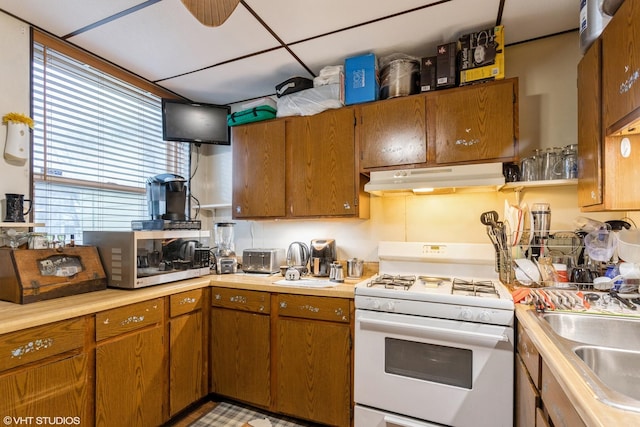 kitchen with white gas stove, light countertops, under cabinet range hood, and a sink