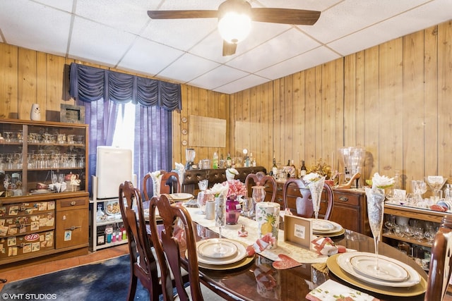 dining area featuring wooden walls, a ceiling fan, and a drop ceiling