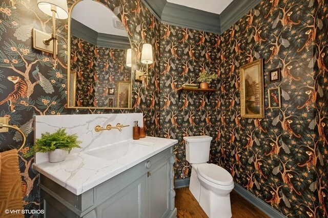 bathroom with vanity, wood finished floors, wallpapered walls, ornamental molding, and toilet