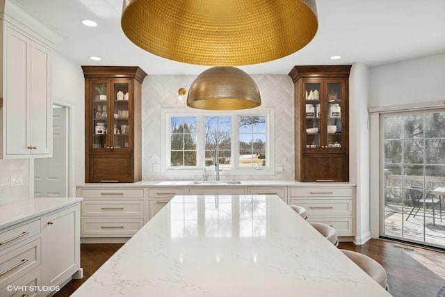 kitchen featuring light stone counters, glass insert cabinets, recessed lighting, and a sink