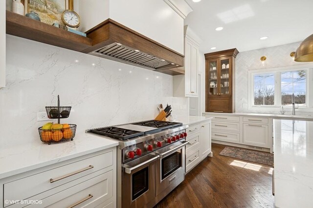 kitchen featuring range with two ovens, light stone countertops, custom range hood, and a sink