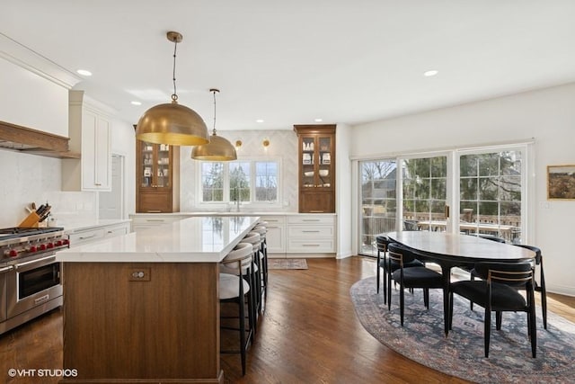 kitchen featuring double oven range, tasteful backsplash, light countertops, glass insert cabinets, and dark wood-style flooring