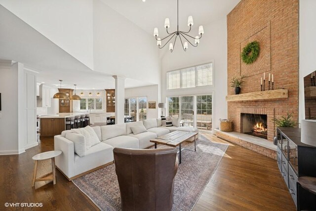 living area featuring dark wood-style floors, a chandelier, a fireplace, and decorative columns