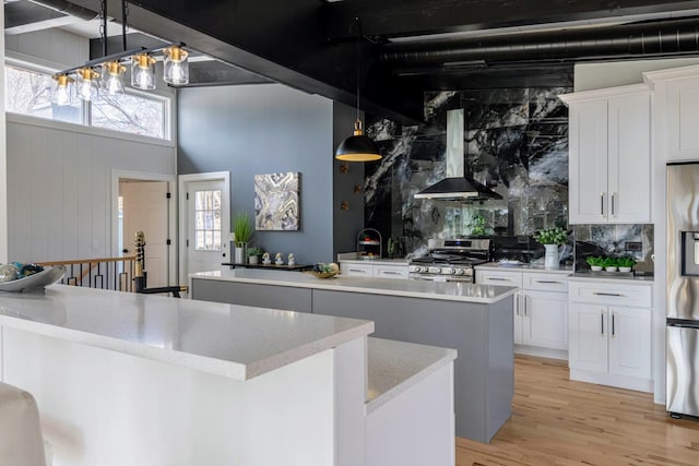 kitchen featuring a kitchen island, light wood-style flooring, stainless steel appliances, wall chimney range hood, and tasteful backsplash