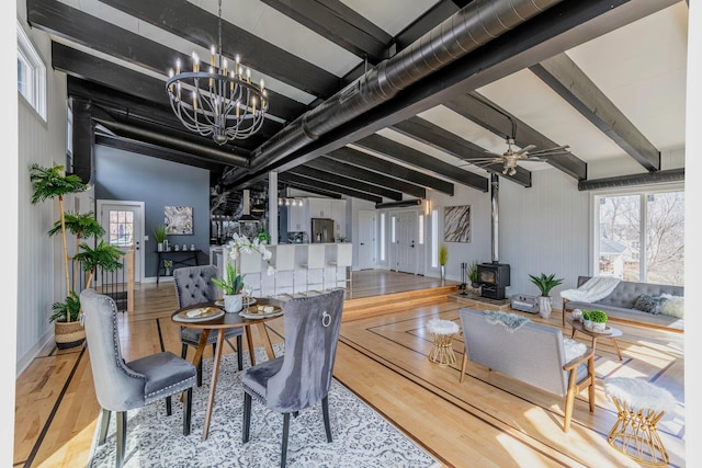 dining space with beam ceiling, wood finished floors, and a wood stove