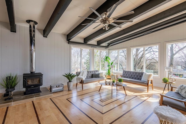 living room with hardwood / wood-style floors, a wood stove, a ceiling fan, and beamed ceiling