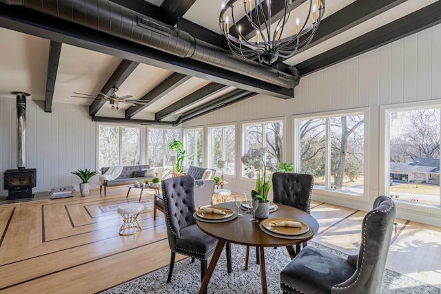 sunroom / solarium with beam ceiling, ceiling fan, and a wood stove