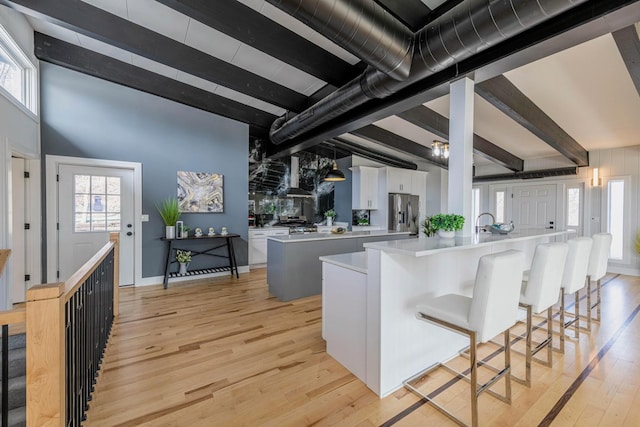 kitchen featuring beam ceiling, light countertops, white cabinets, light wood-style floors, and wall chimney exhaust hood