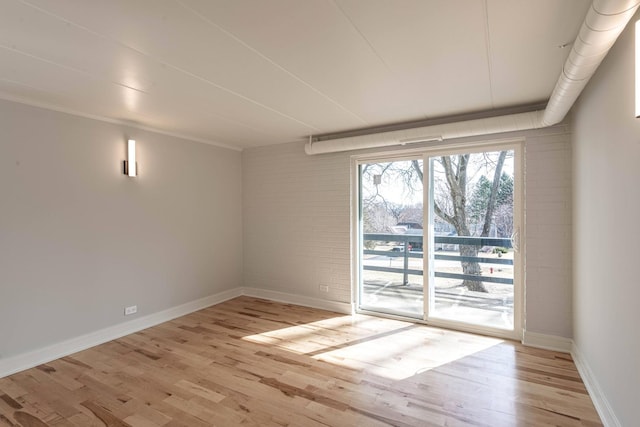 empty room with baseboards, light wood-type flooring, and brick wall