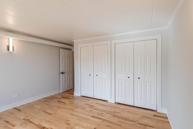 unfurnished bedroom featuring baseboards, multiple closets, light wood-style floors, and ornamental molding