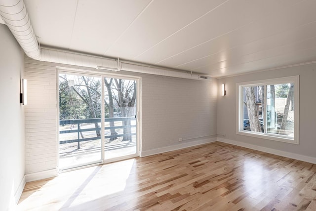 unfurnished room with light wood-style flooring, baseboards, and brick wall