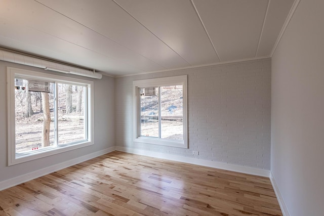 unfurnished room with crown molding, a wealth of natural light, light wood-style flooring, and brick wall