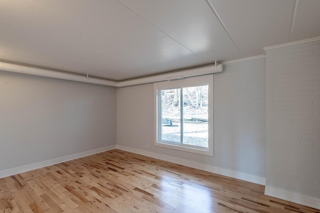 unfurnished room featuring light wood-type flooring, baseboards, and brick wall