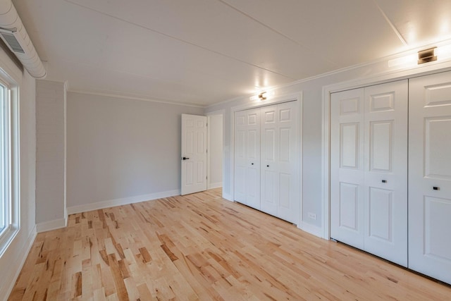 unfurnished bedroom with crown molding, baseboards, light wood-style floors, and multiple closets