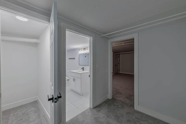 hallway featuring a sink, baseboards, and light carpet