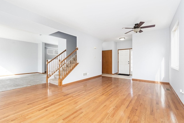 unfurnished living room featuring stairway, baseboards, and light wood finished floors