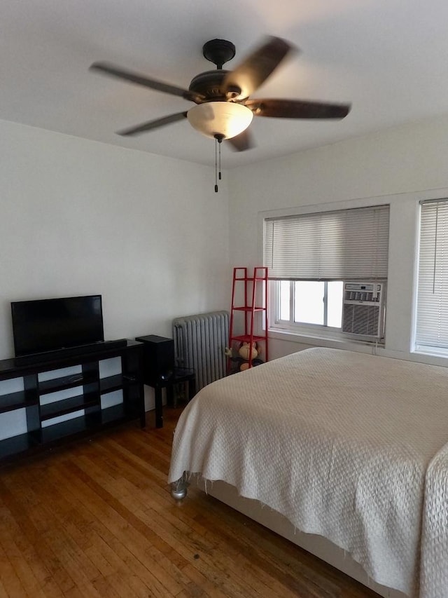 bedroom featuring cooling unit, a ceiling fan, radiator heating unit, and hardwood / wood-style flooring