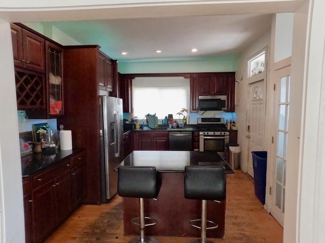 kitchen featuring a kitchen island, appliances with stainless steel finishes, a kitchen bar, dark countertops, and light wood-type flooring