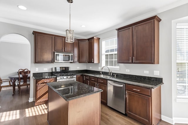 kitchen featuring dark stone countertops, light wood finished floors, ornamental molding, a sink, and appliances with stainless steel finishes