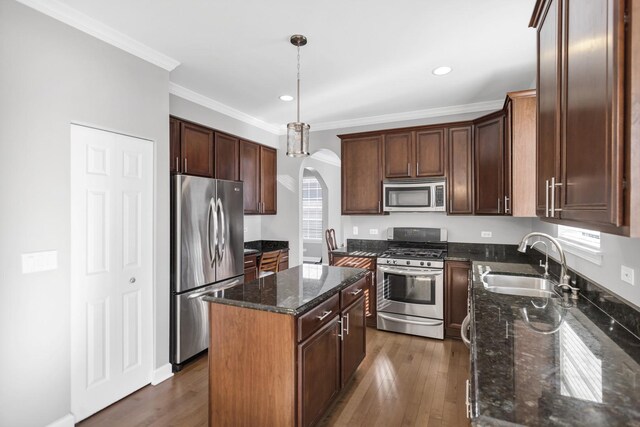 kitchen featuring a sink, a center island, stainless steel appliances, arched walkways, and dark stone counters