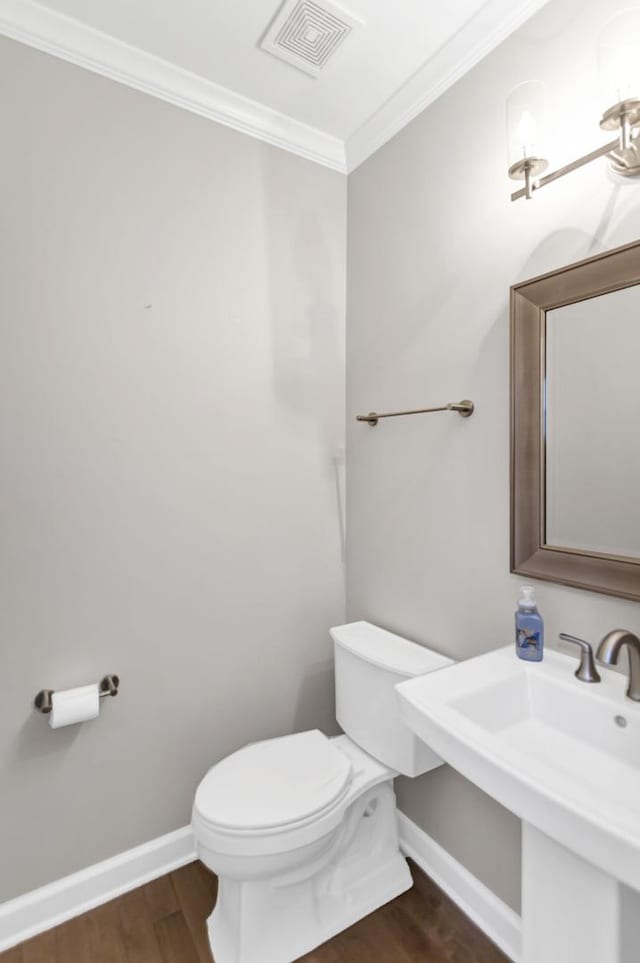 half bath with visible vents, crown molding, baseboards, toilet, and wood finished floors