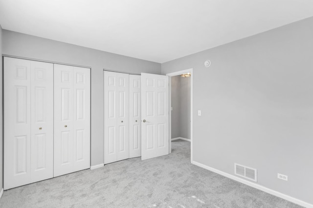 unfurnished bedroom with baseboards, visible vents, two closets, and carpet