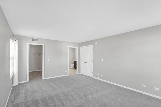 unfurnished bedroom with baseboards, visible vents, carpet floors, a closet, and a walk in closet