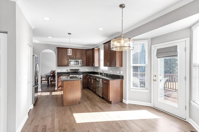 kitchen with light wood-type flooring, a sink, a kitchen island, dark countertops, and appliances with stainless steel finishes