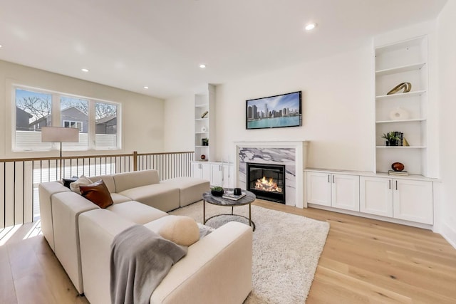 living room featuring a high end fireplace, recessed lighting, built in shelves, and light wood-style floors