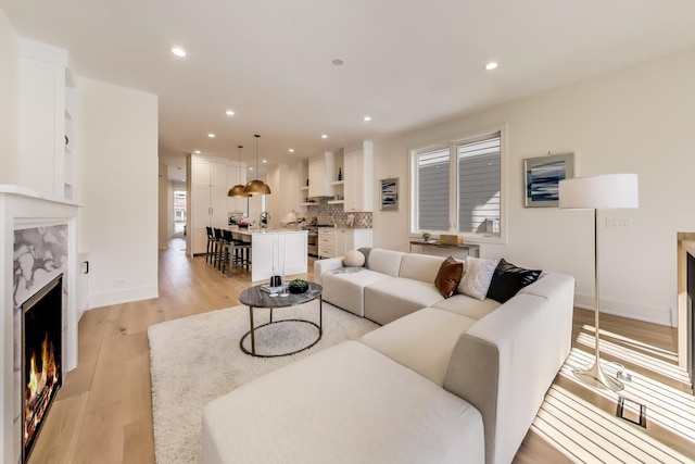 living area featuring baseboards, recessed lighting, light wood-type flooring, and a premium fireplace