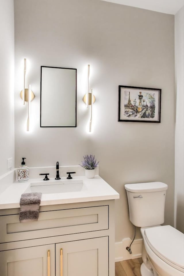 half bathroom with baseboards, toilet, wood finished floors, and vanity