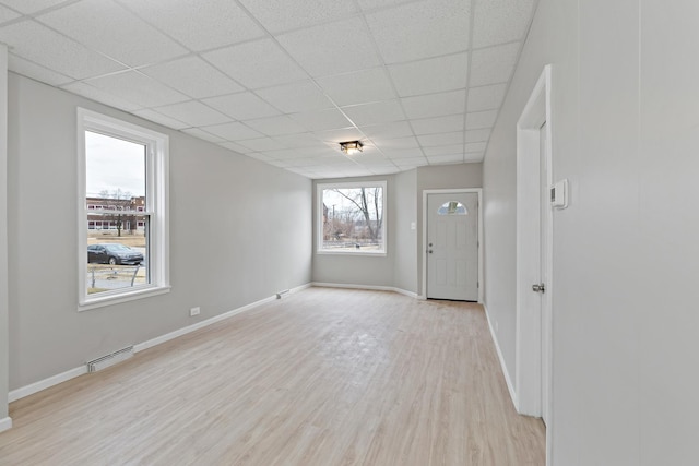 spare room featuring a baseboard heating unit, a drop ceiling, baseboards, and light wood finished floors