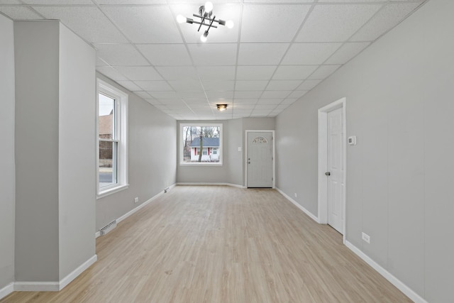 spare room with baseboards, a paneled ceiling, and light wood finished floors