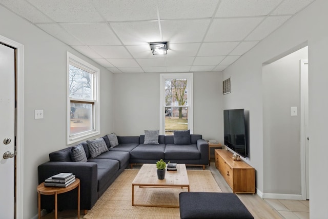 living room with a wealth of natural light, visible vents, baseboards, and a drop ceiling