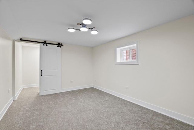 carpeted empty room featuring a barn door and baseboards