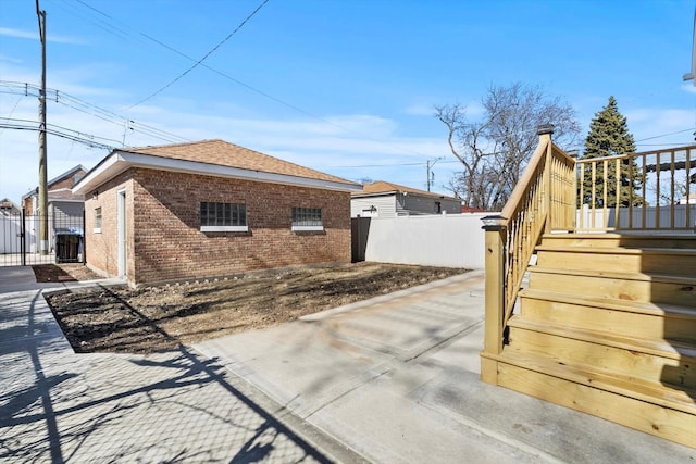 view of property exterior featuring brick siding, a shingled roof, stairs, and fence