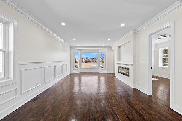 unfurnished living room featuring a decorative wall, ornamental molding, recessed lighting, a glass covered fireplace, and dark wood-style flooring