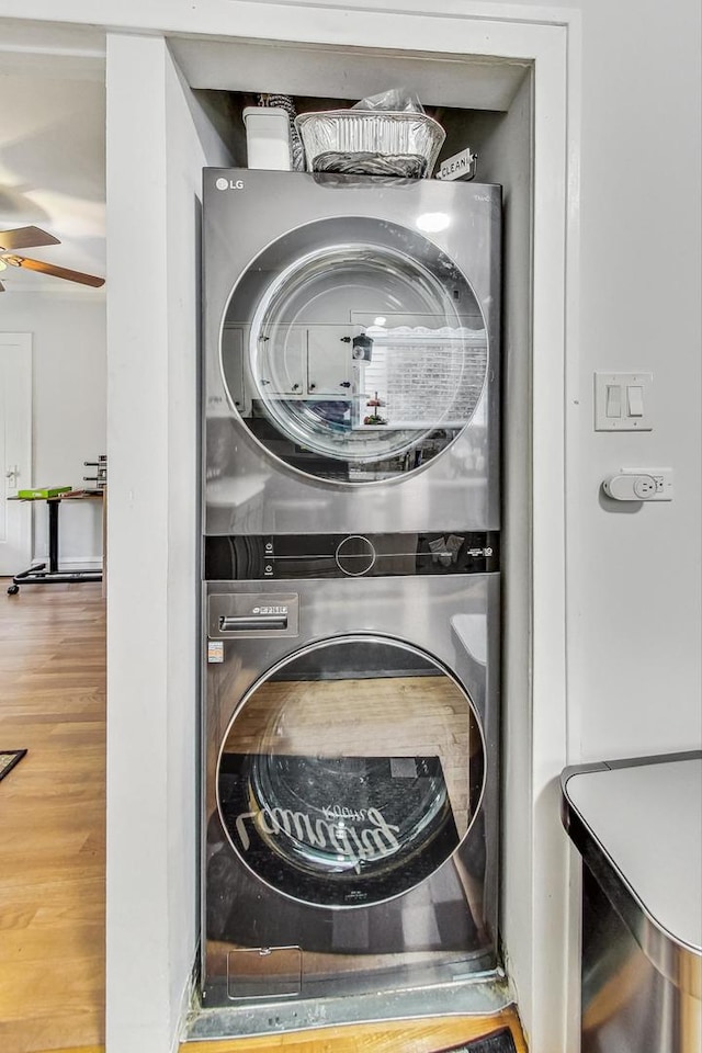 washroom featuring laundry area, stacked washing maching and dryer, a ceiling fan, and wood finished floors