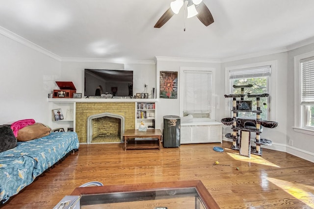 living room with wood finished floors, baseboards, a ceiling fan, a fireplace, and crown molding