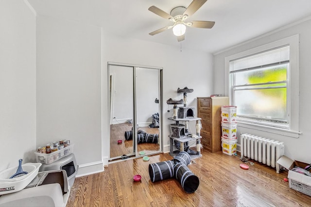 exercise area featuring radiator, wood finished floors, baseboards, and ceiling fan