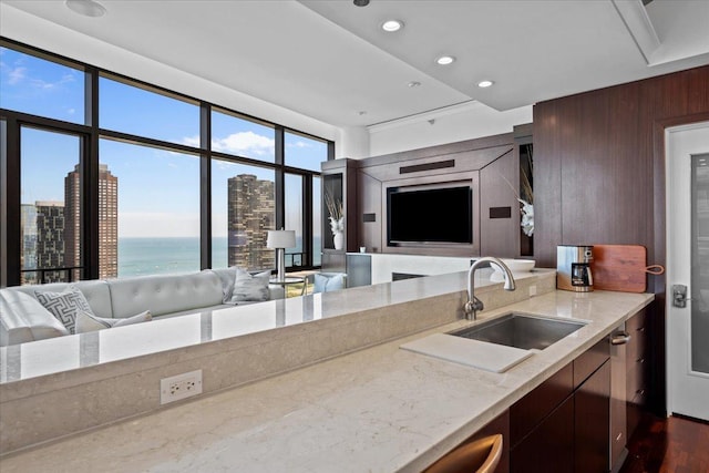 kitchen with a sink, light stone counters, wooden walls, and open floor plan