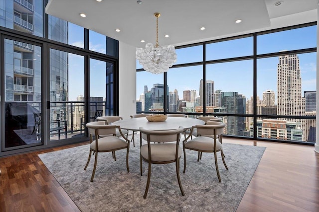 dining area with wood finished floors, a healthy amount of sunlight, an inviting chandelier, floor to ceiling windows, and a view of city