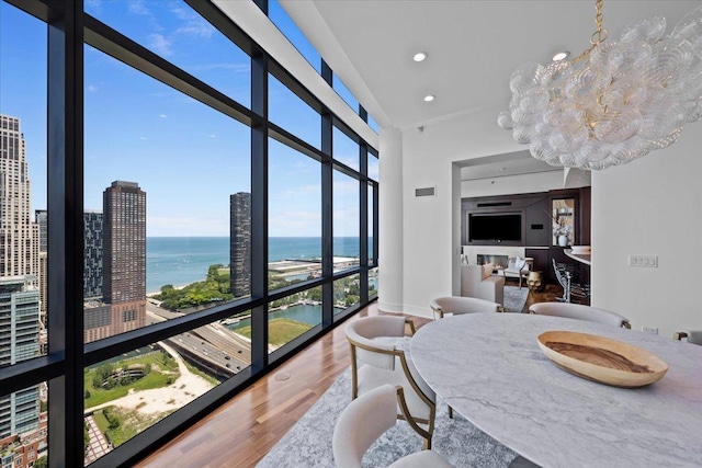 dining space featuring wood finished floors, recessed lighting, a lit fireplace, a wall of windows, and a chandelier