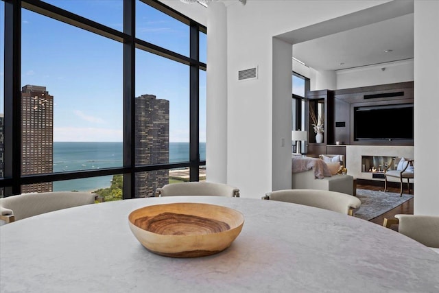 dining room featuring visible vents, a water view, wood finished floors, a high end fireplace, and a wall of windows