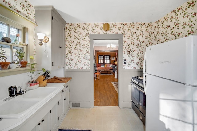 kitchen featuring visible vents, a wainscoted wall, wallpapered walls, freestanding refrigerator, and range with gas cooktop