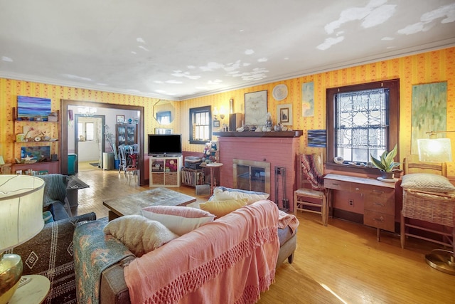 living area featuring a brick fireplace, wood finished floors, crown molding, and wallpapered walls